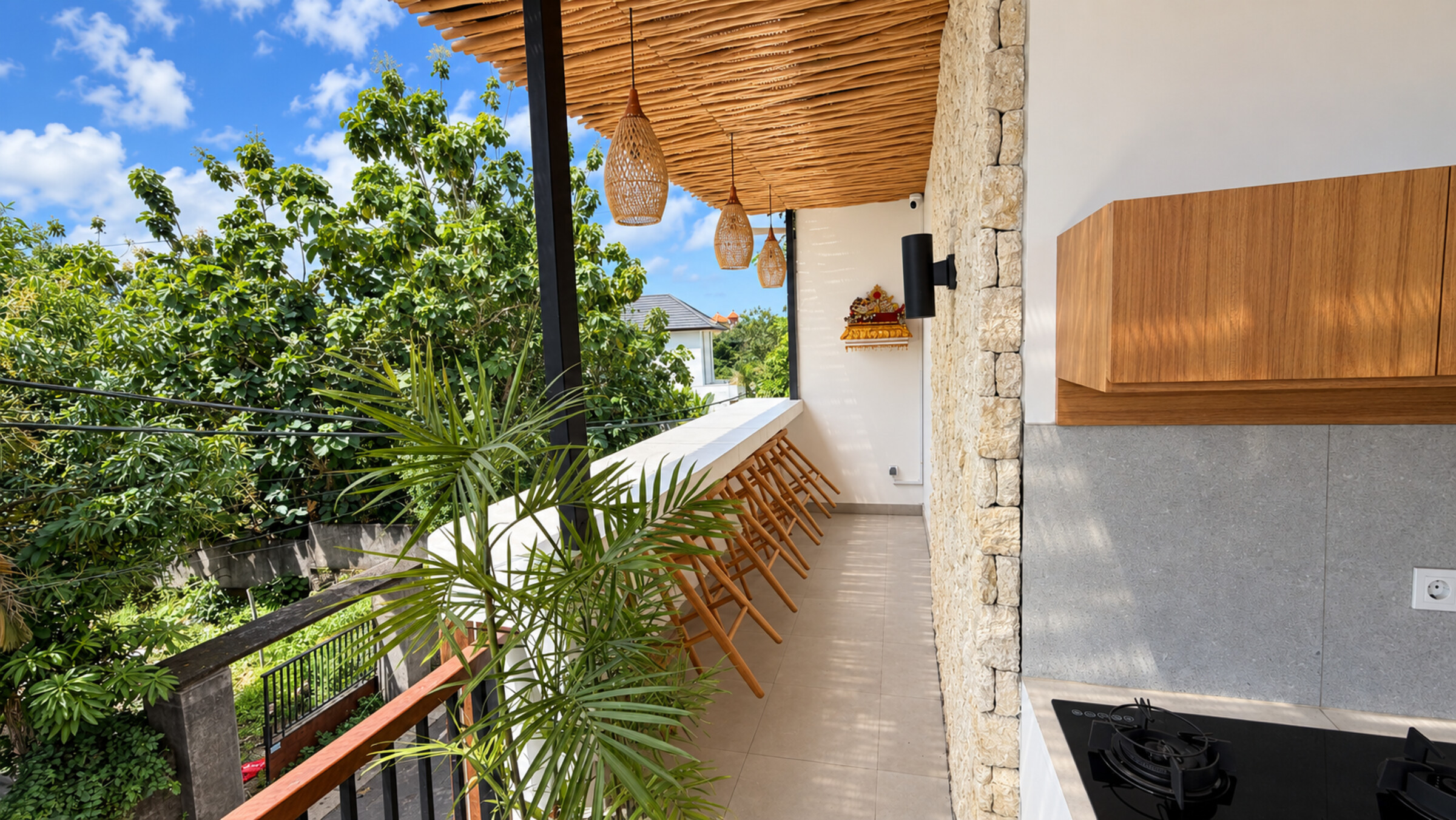 Covered balcony with wooden stools, hanging lamps, greenery and a kitchenette